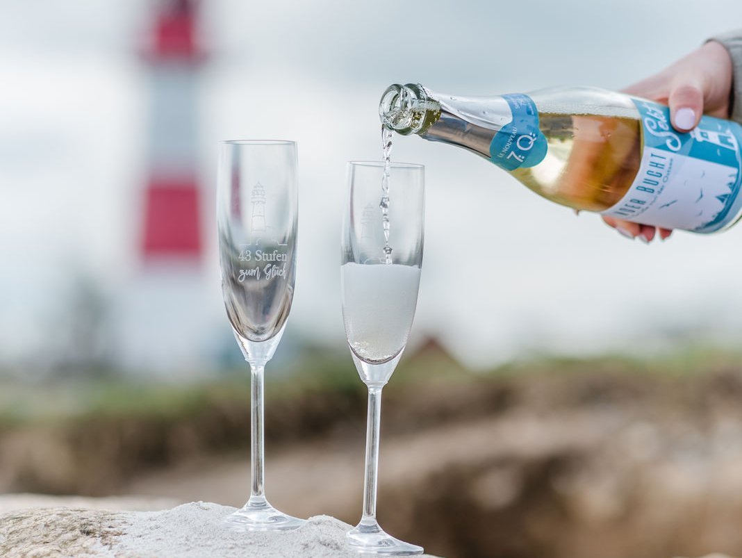 Sekt, der in 2 Gläser eingegossen wird mit dem Leuchtturm im Hintergrund