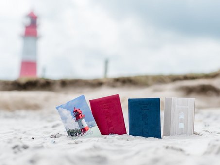 Stammesbücher im Sand mit Leuchtturm im Hintergrund